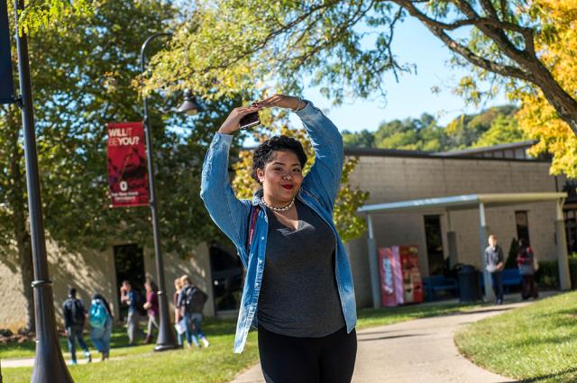 A woman stands outside, holding her arms in a "letter O" position