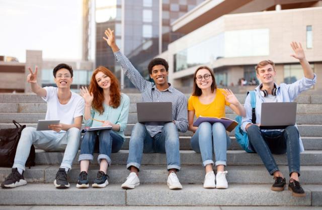 students sitting on steps with hand in the air, and laptops