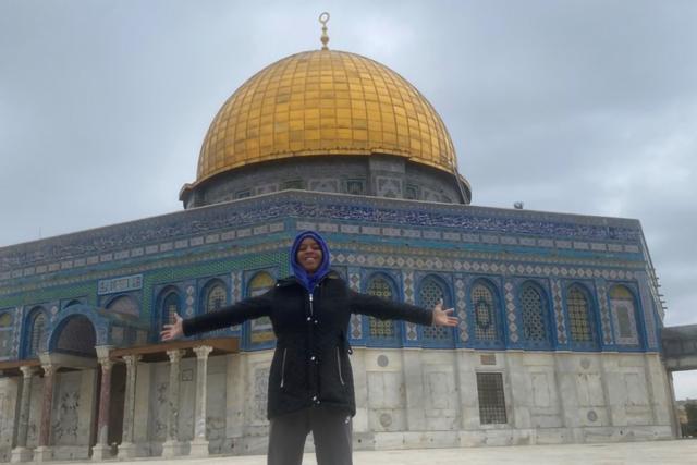 Student in warm jacket stands in front of a white building with a gold-tiled dome