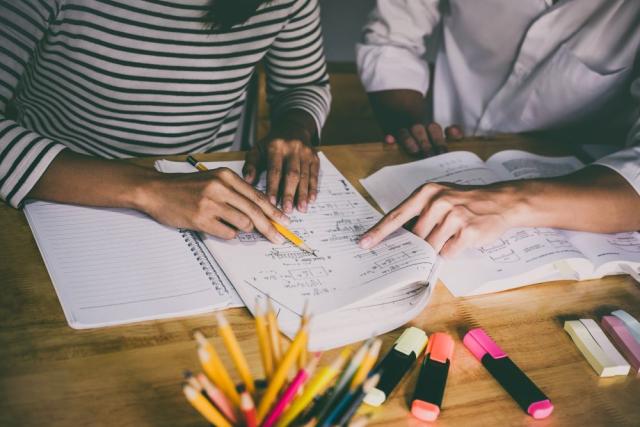 two people working on math problem with lots of pencils and highlighters nearby