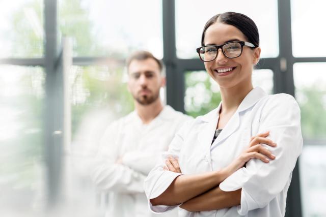 Woman scientist in white lab coat stands in front of a male scientist in the backgrouns