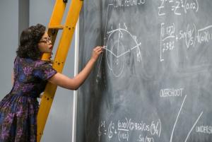 A Black woman writes math equations on a chalkboard