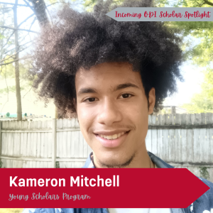 Kameron Mitchel, a man of color, stands in front of a wooden fence in a blue shirt