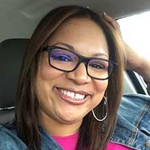 Donya Gilmore smiling with black glasses and a bright pink shirt